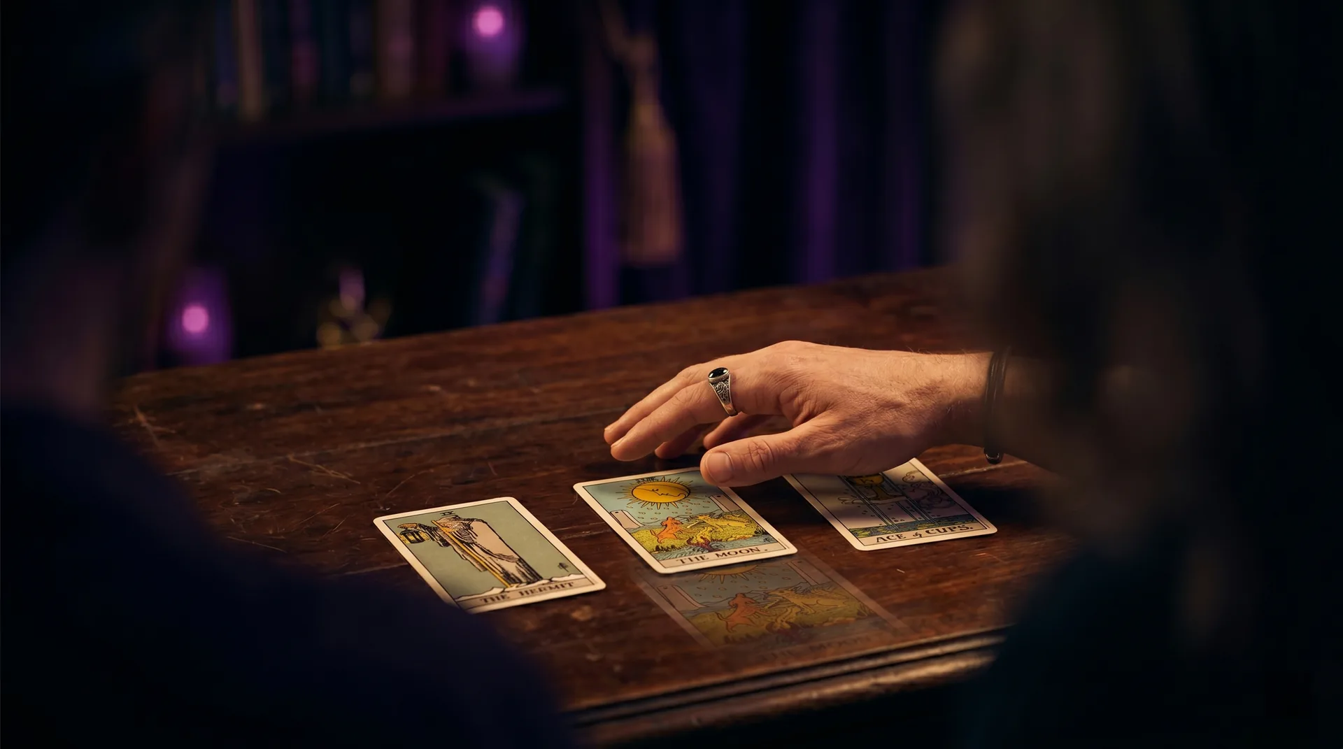Una persona observando cartas de Tarot iluminadas sobre una mesa oscura, en actitud reflexiva
